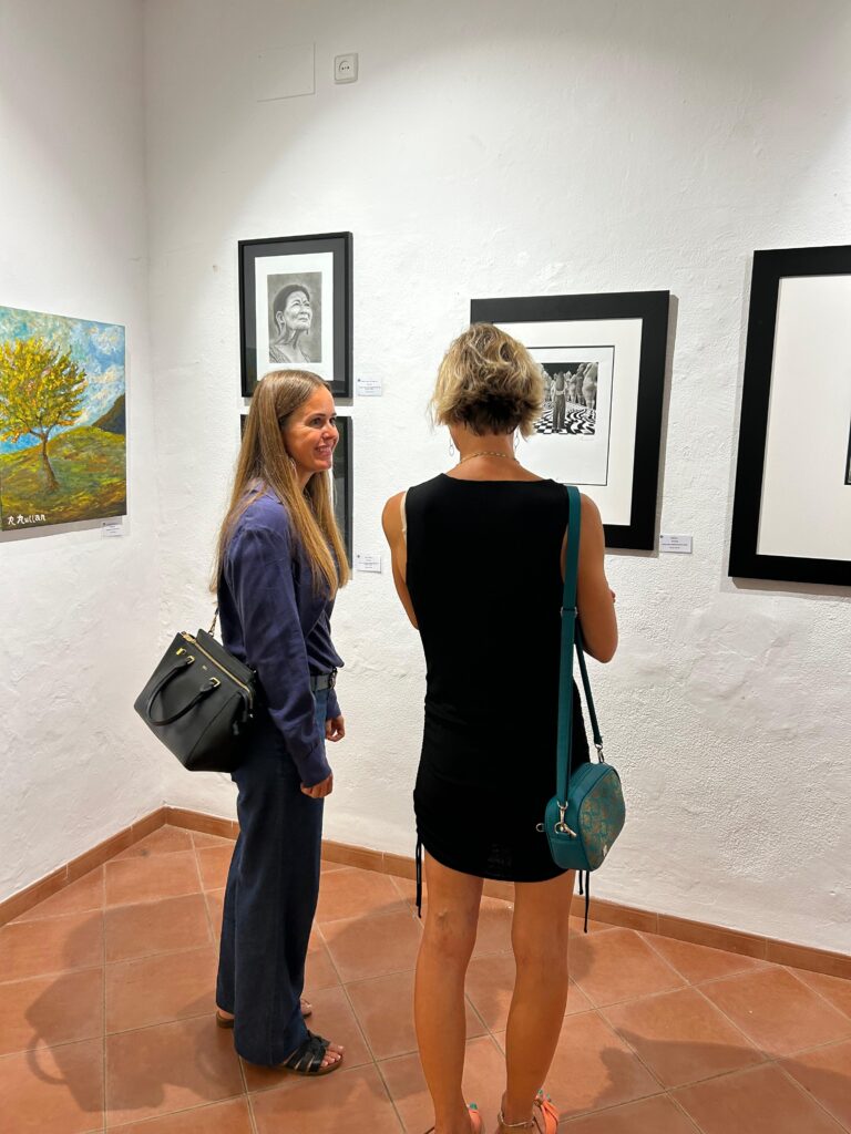 Visitors viewing charcoal and graphite portrait drawings by Janis Baer at group exhibition in Museu de Sóller, Mallorca