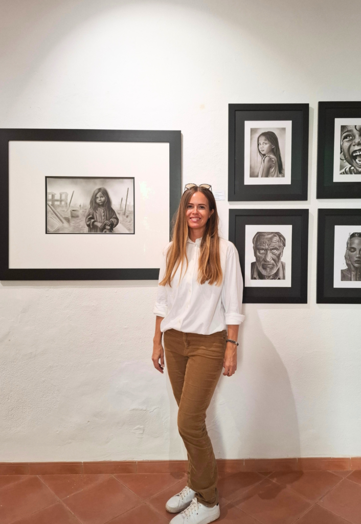Contemporary artist Janis Bär standing beside her exhibited charcoal drawings during the Artists of Mallorca Autumn Exhibition 2025 at Museu de Sóller, Mallorca.