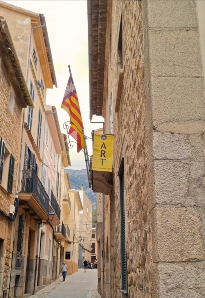 Historic street in Sóller, Mallorca, with exhibition signage and flags outside Museu de Sóller during the Artists of Mallorca Autumn Exhibition 2025.